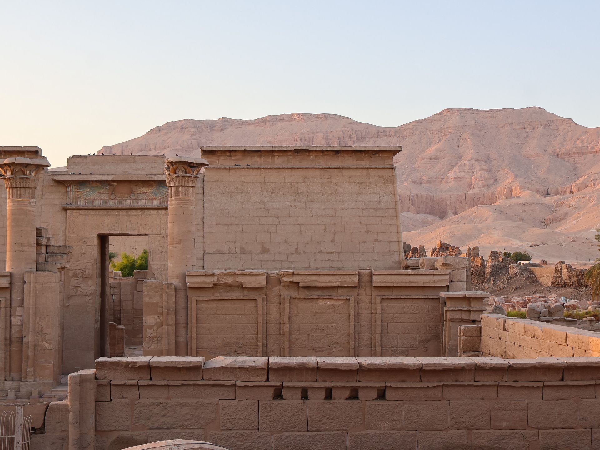 Ancient Egyptian temple ruins in tan stone, with mountains in the background.