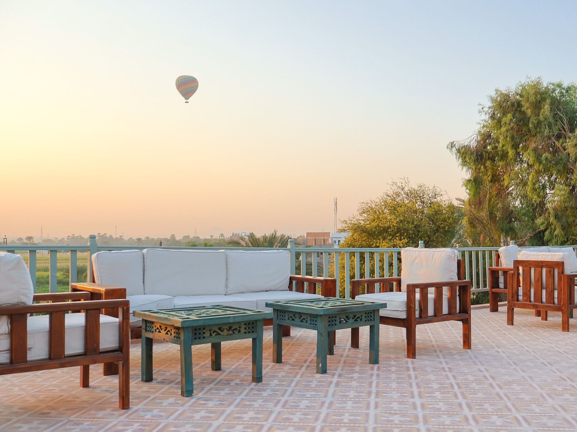 Outdoor seating area with couches and tables, hot air balloon in the sky during sunrise.