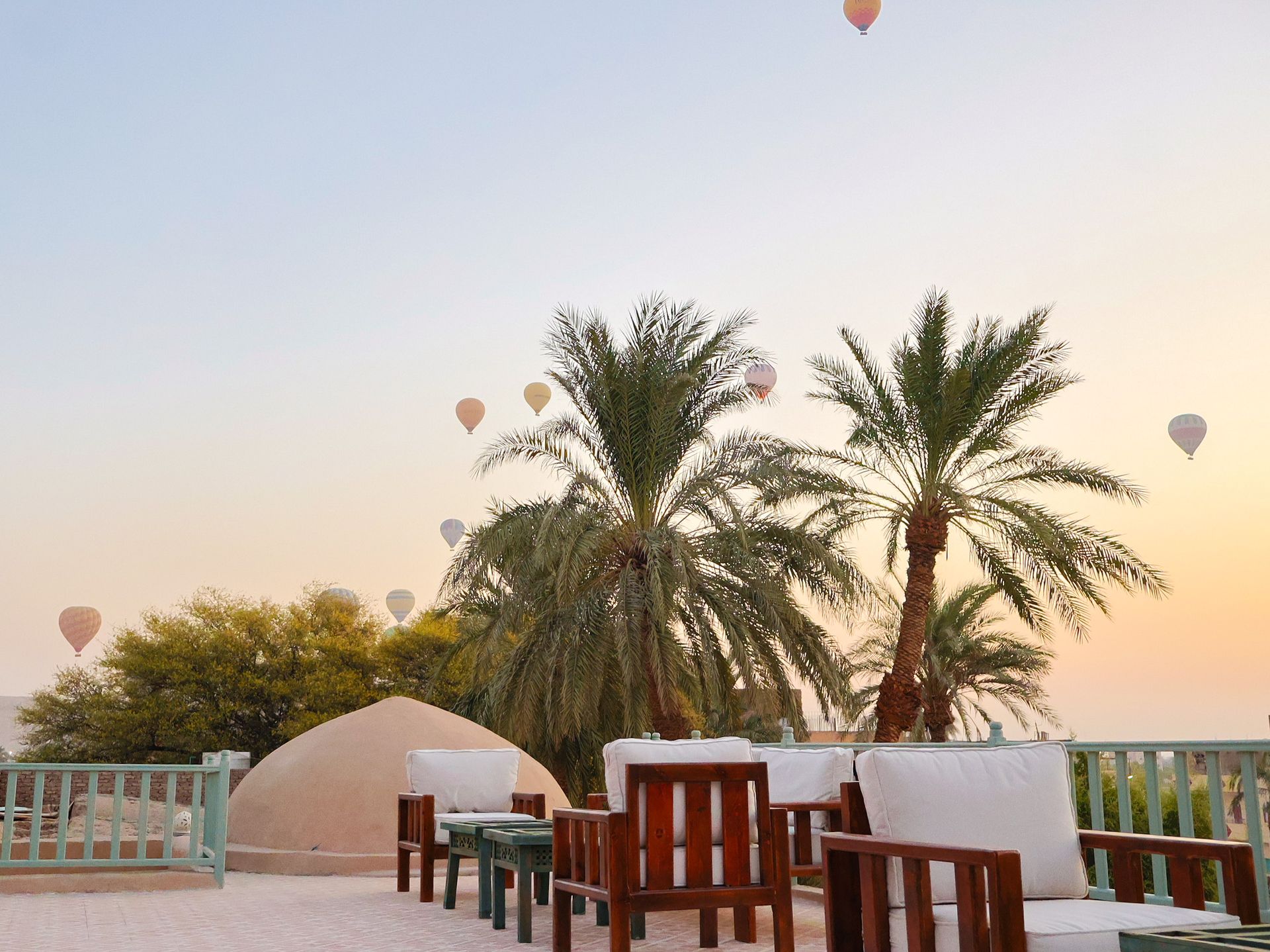 Rooftop seating with palm trees, hot air balloons in sky at dawn.
