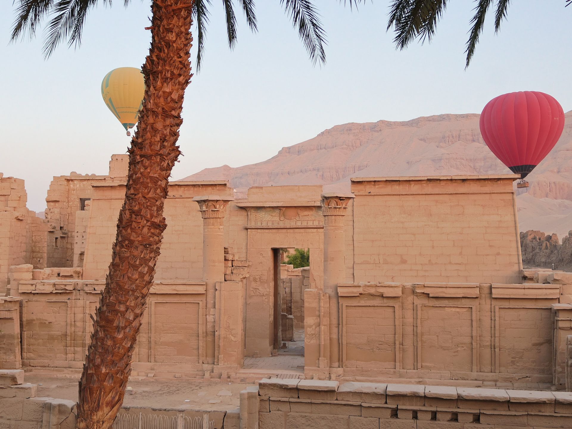 Ancient temple with two hot air balloons in the air, palm tree in the foreground.