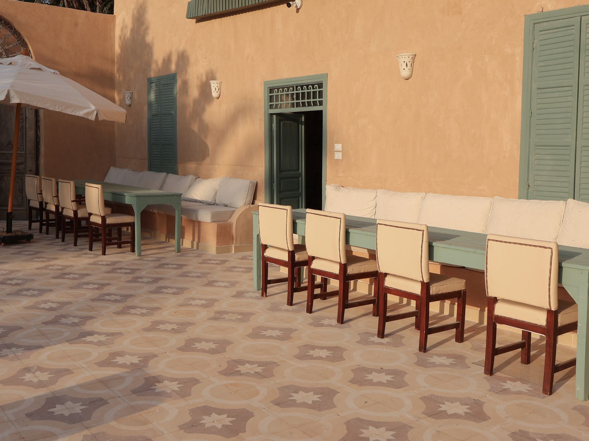 Outdoor seating area with tiled floor, peach walls, teal shutters/trim, and cream-colored furniture.