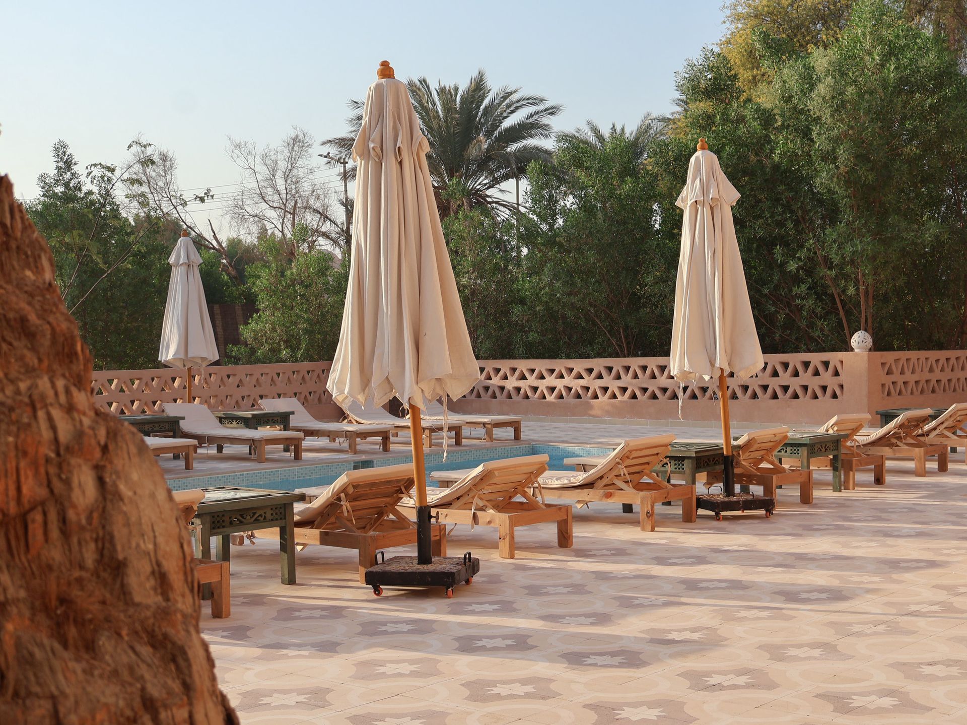 Swimming pool with lounge chairs and umbrellas, trees in the background, sunny day.