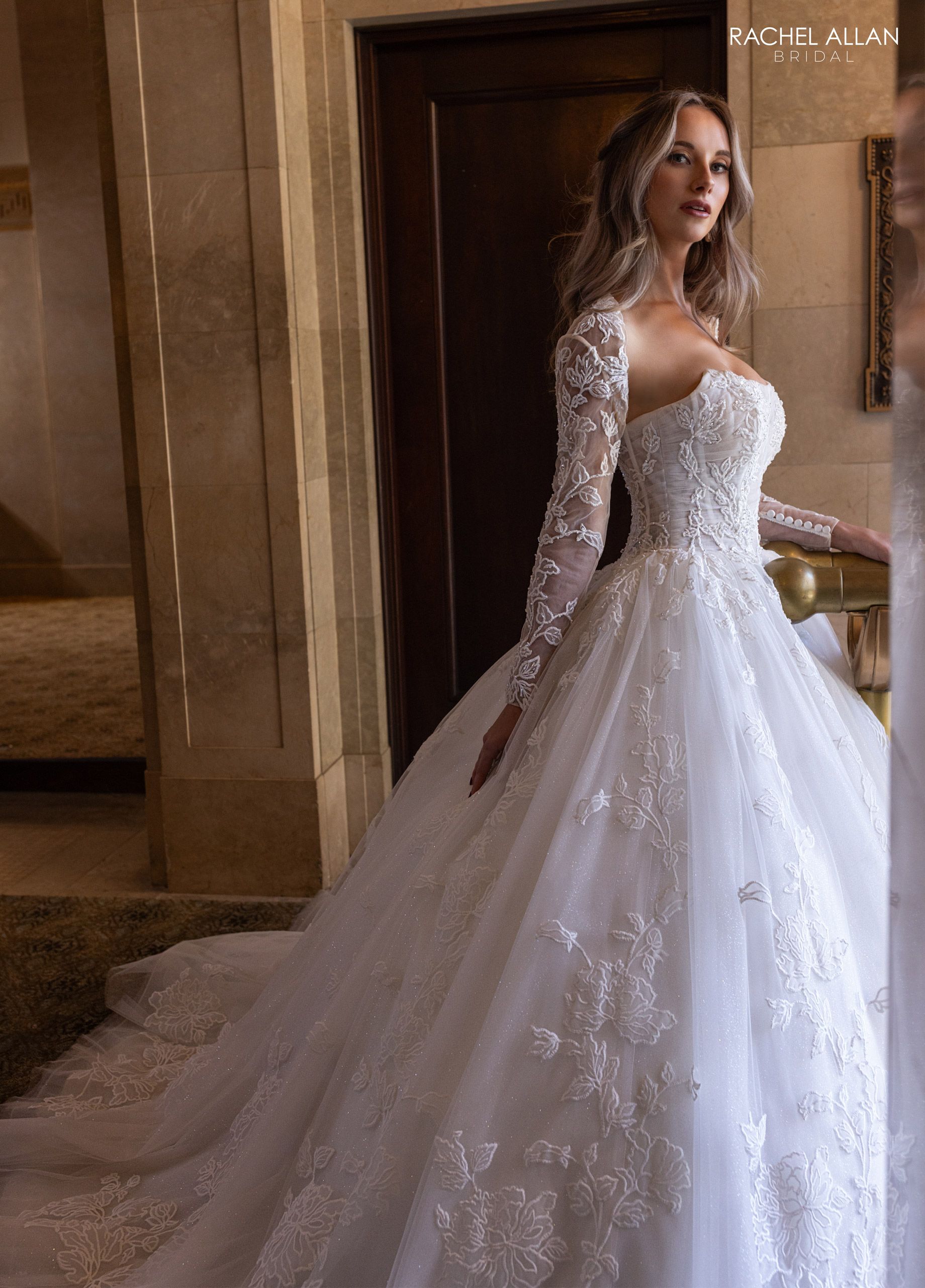 Woman in white wedding dress with long sleeves, standing near doorway.