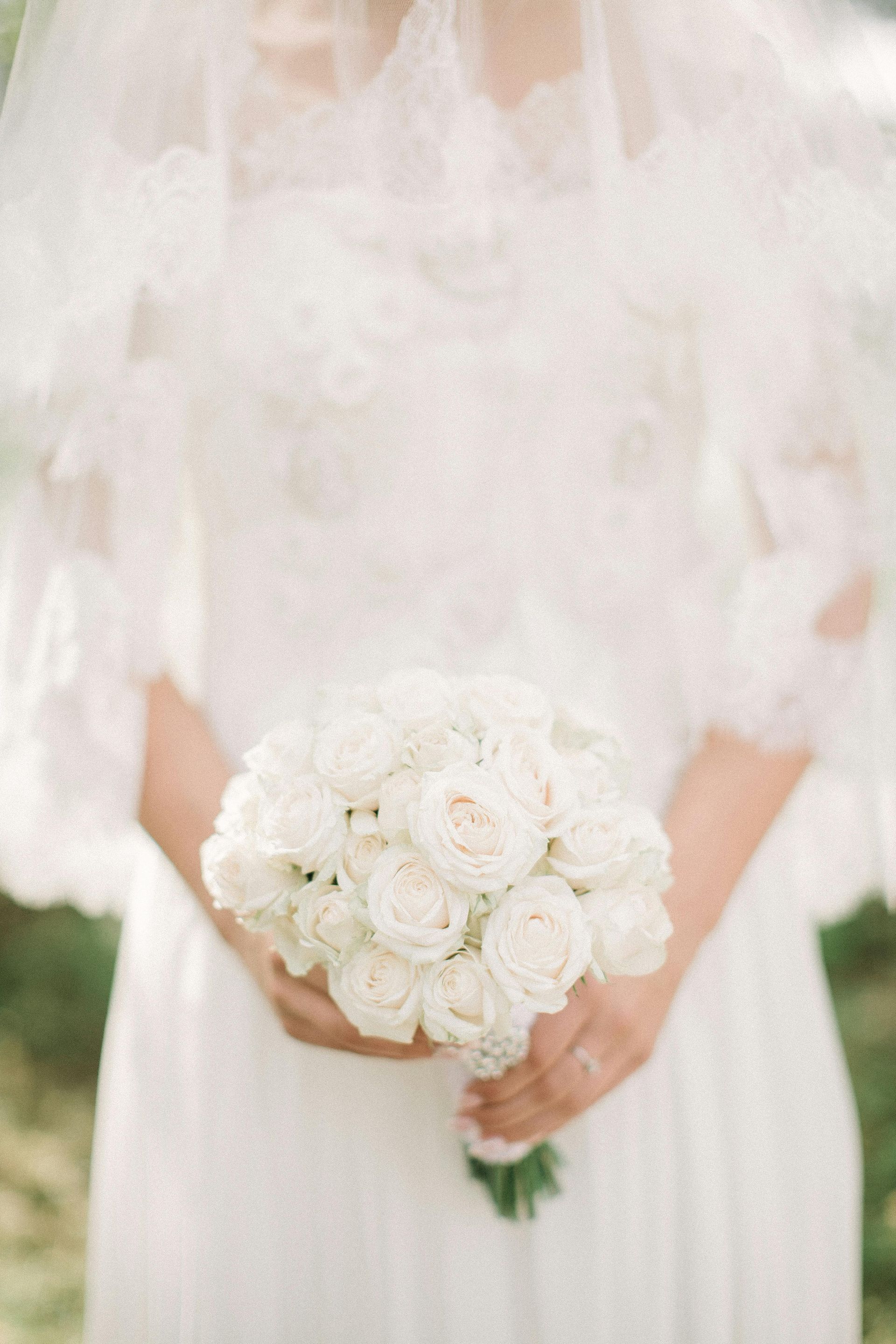 Bride in a white dress holding a bouquet of white roses, partially obscured by veil.