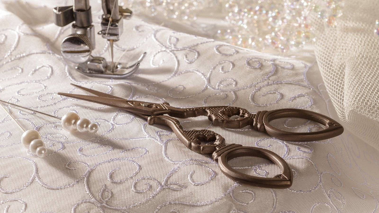 Sewing machine, ornate scissors, pearls, and fabric with floral embroidery.