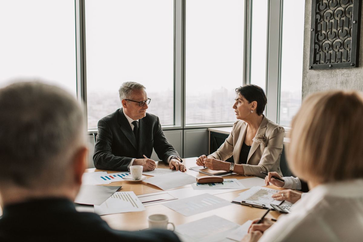 People in a business meeting around a conference table, discussing documents in a bright office.