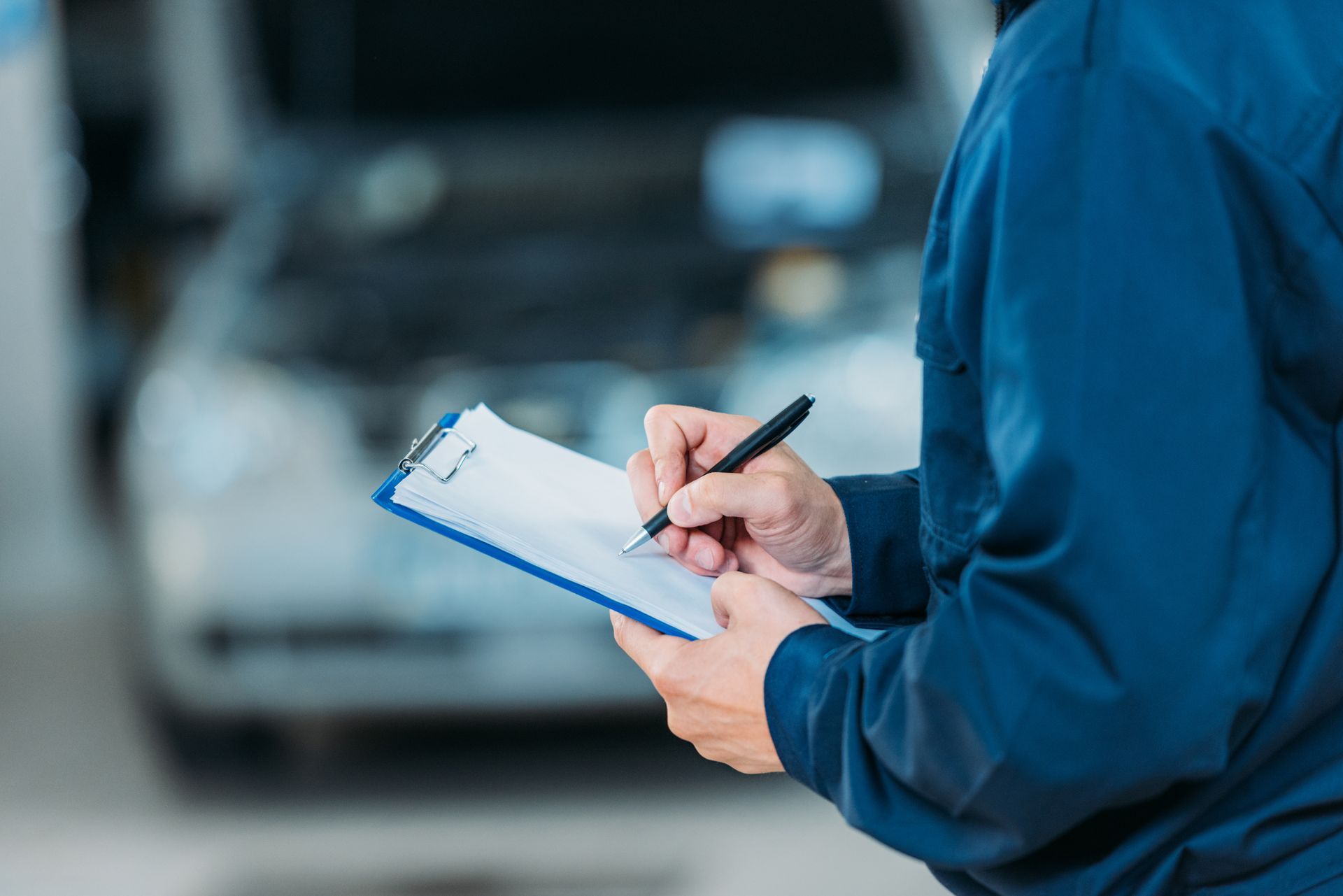 Una persona con una giacca blu scrive su un blocco appunti accanto a un'auto sfocata sullo sfondo.