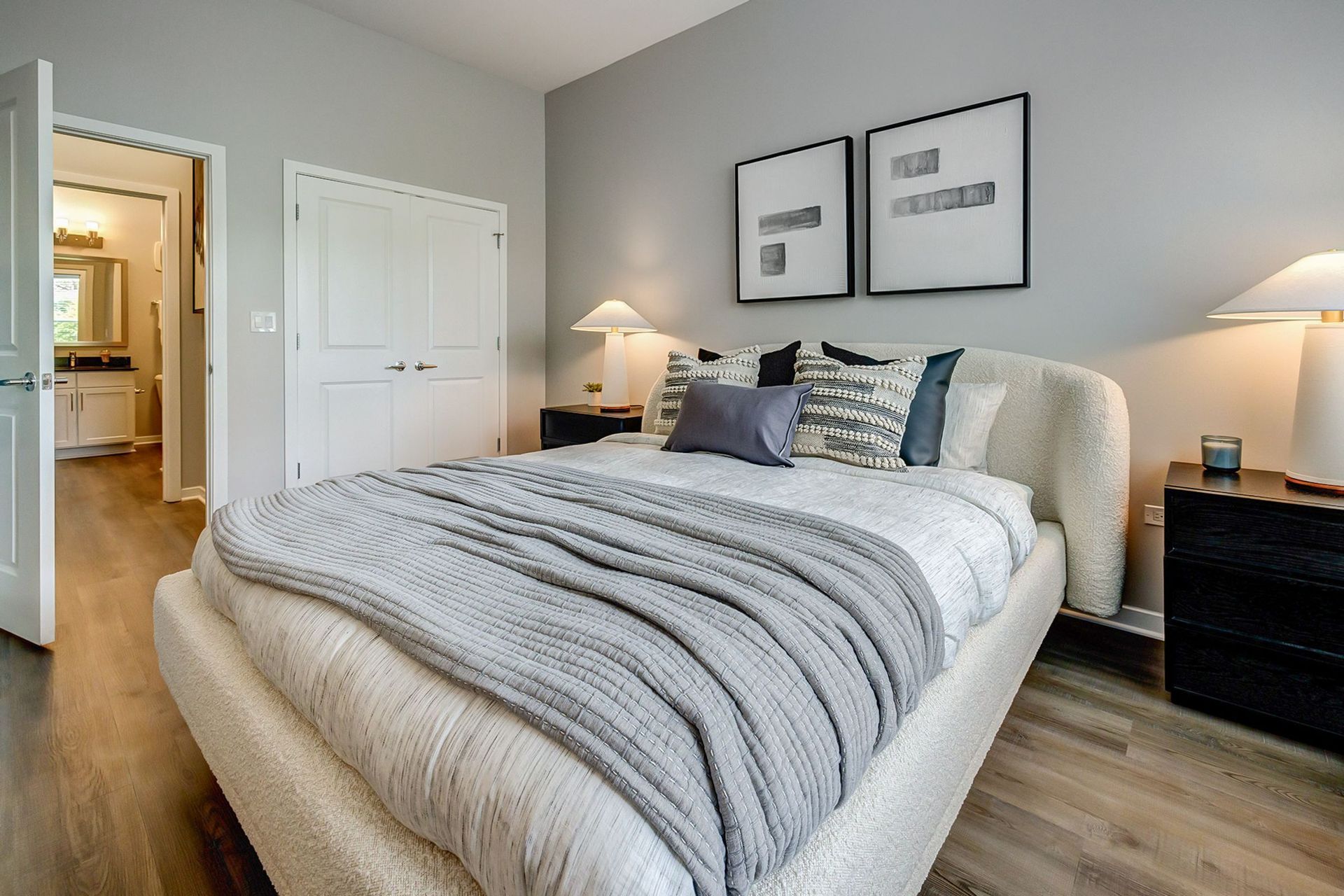 A bedroom with a king size bed , two nightstands , two lamps and two pictures on the wall.