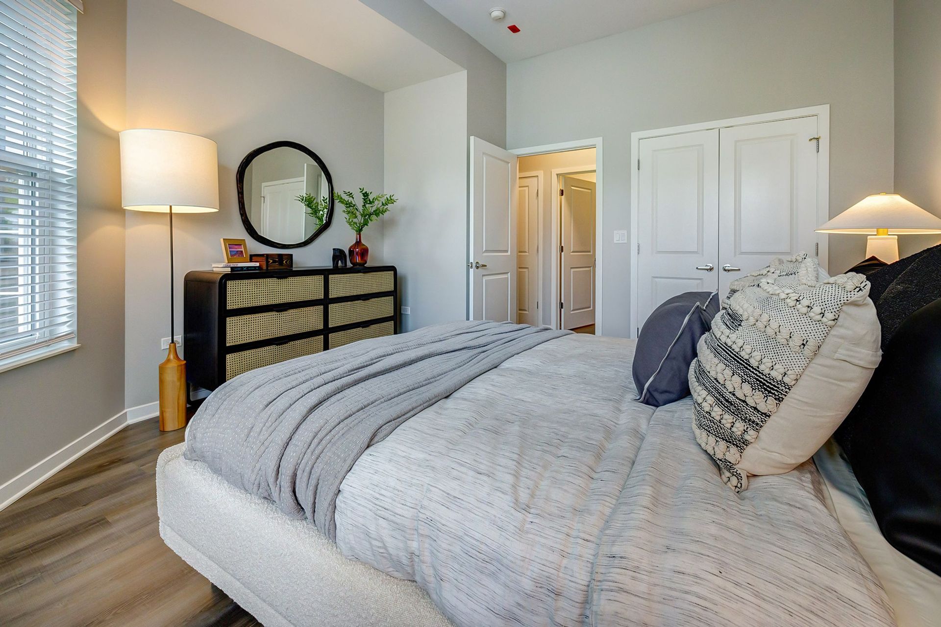 A bedroom with a bed , dresser , lamp and mirror.
