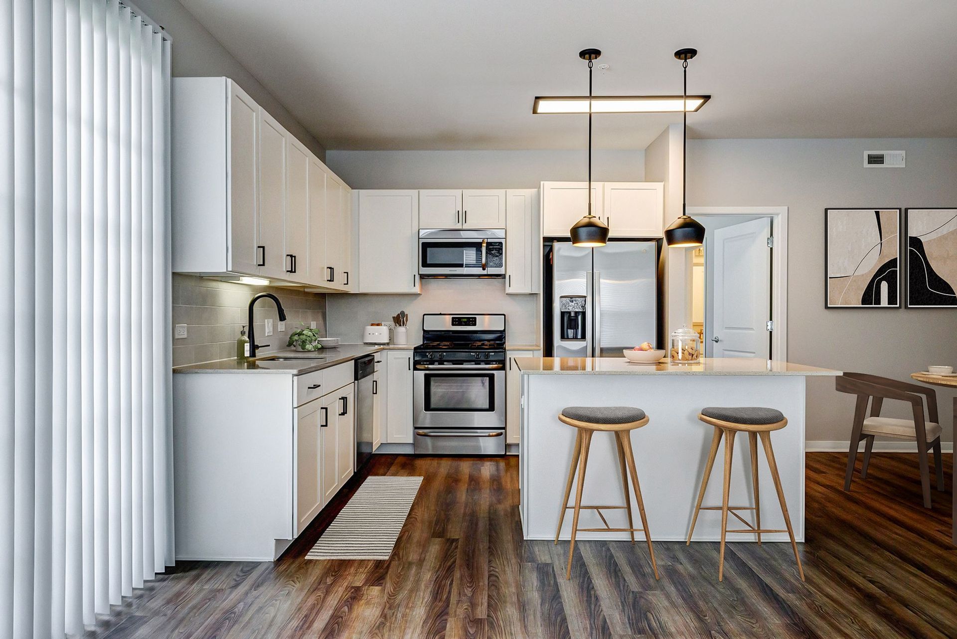 A kitchen with white cabinets , stainless steel appliances , wooden floors and a large island.