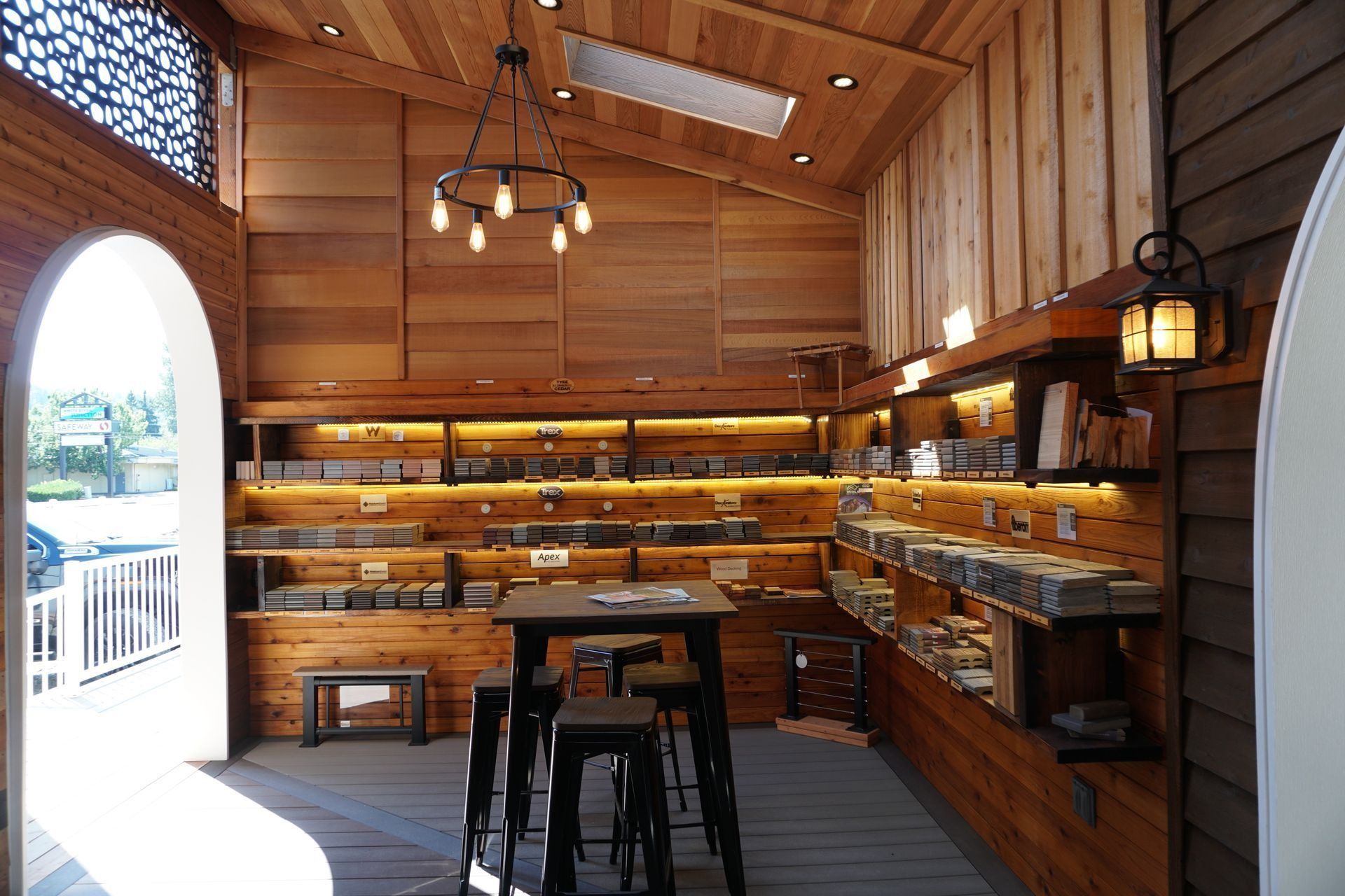 Interior of a wooden shop with shelves of products, a table with stools, and a hanging light fixture.