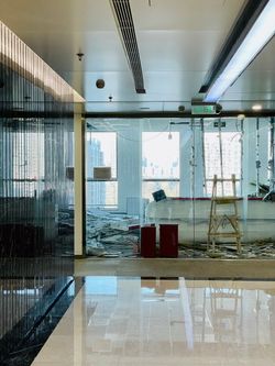 Modern office hallway with glass walls, reflective floor, and construction debris near bright windows