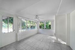 Bright empty sunroom with white tiled floor, large windows, and a ceiling fan.