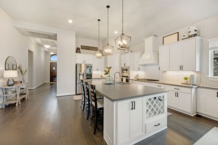 Bright white kitchen with island, chandelier, bar stools, and hardwood floors, opening to a dining area