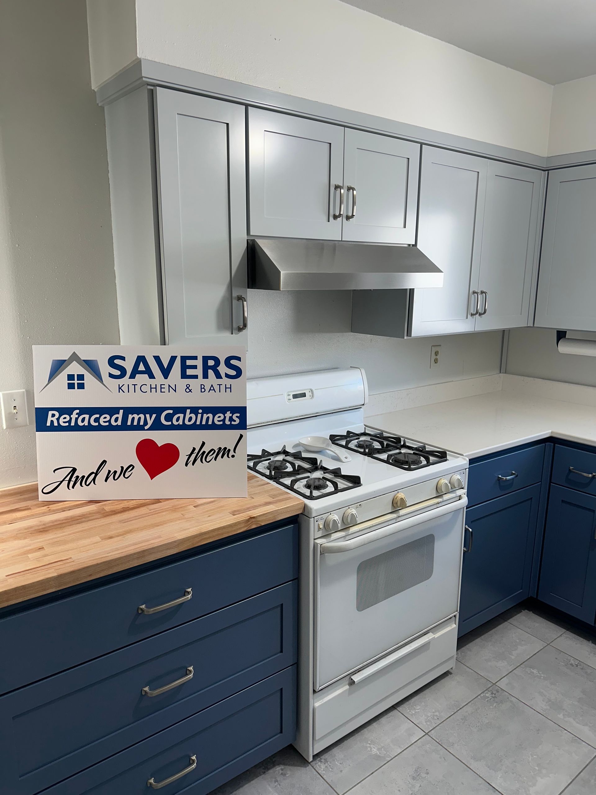 Modern kitchen with gray and blue cabinets, stainless range hood, white stove, and wooden countertop sign.