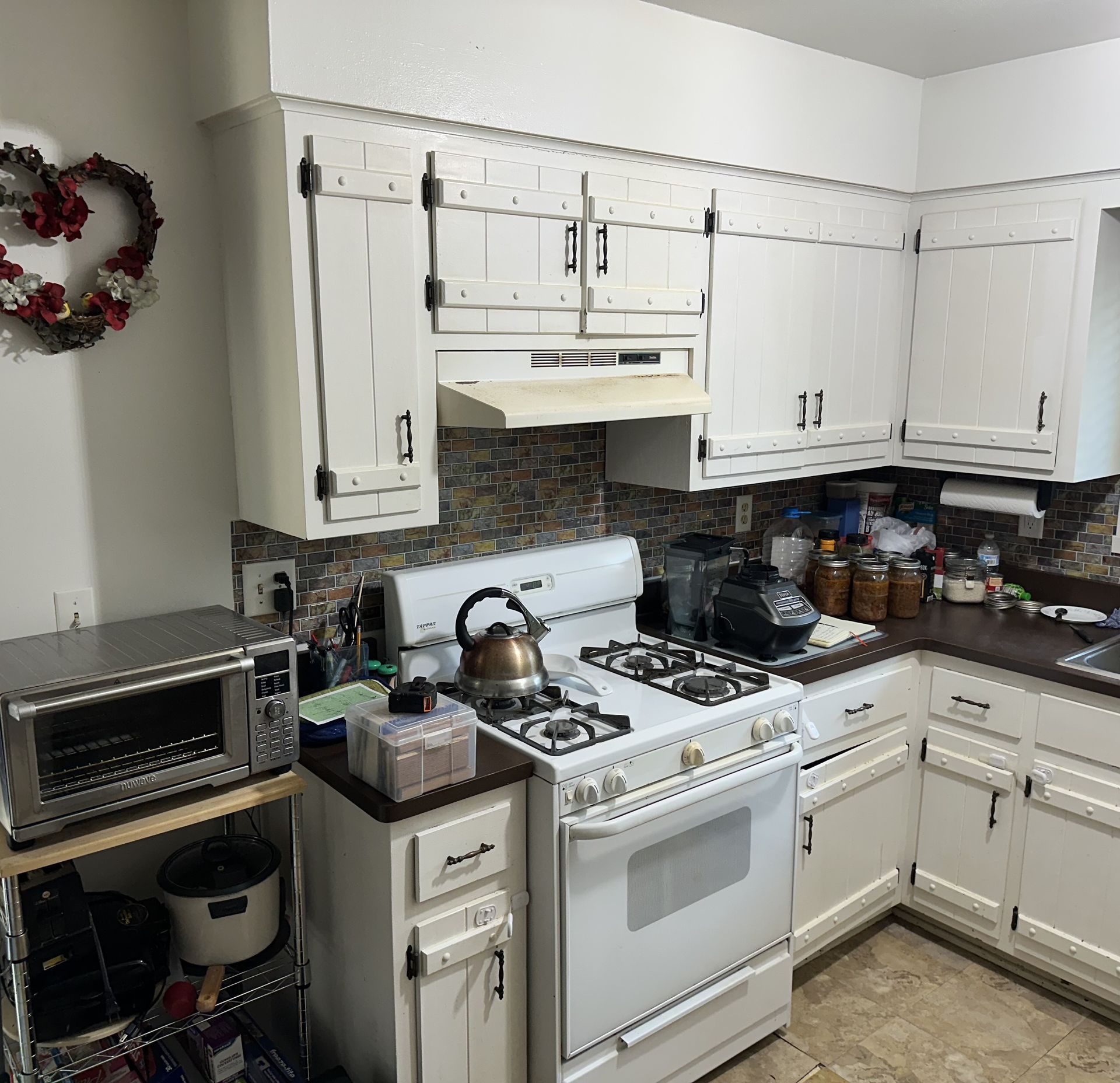 Small white kitchen with stove, microwave, countertops, and hanging wreath on the wall.