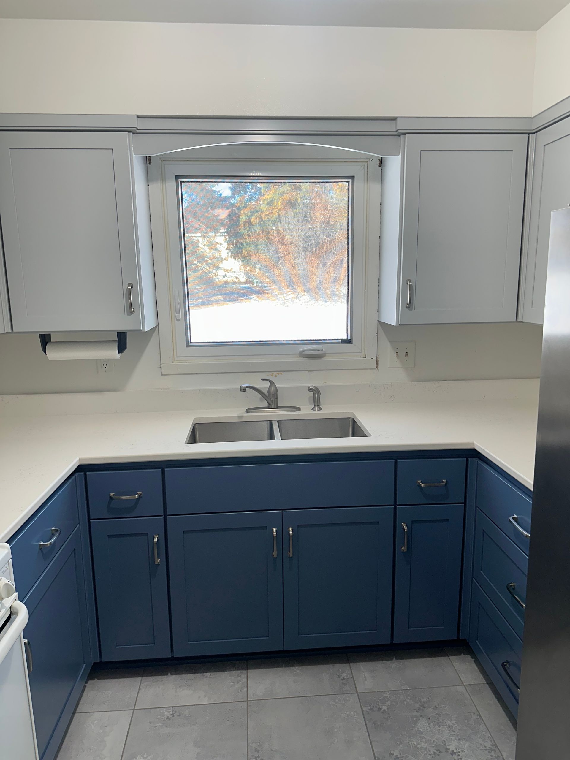 Blue kitchen cabinets and white countertops with a double sink beneath a window.