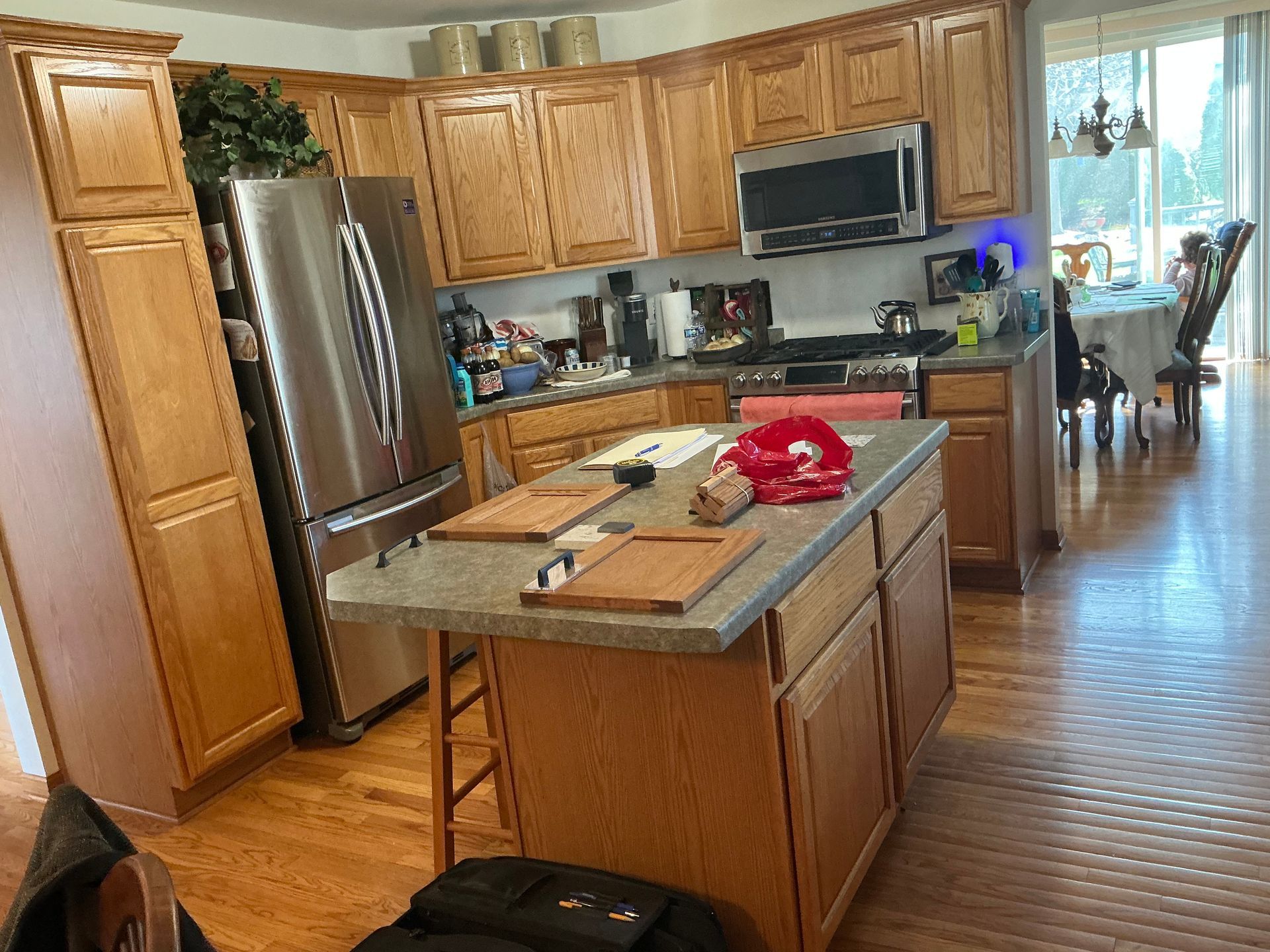 Modern kitchen with wood cabinets, stainless fridge, island, and a red cloth on the counter, opening to a dining area