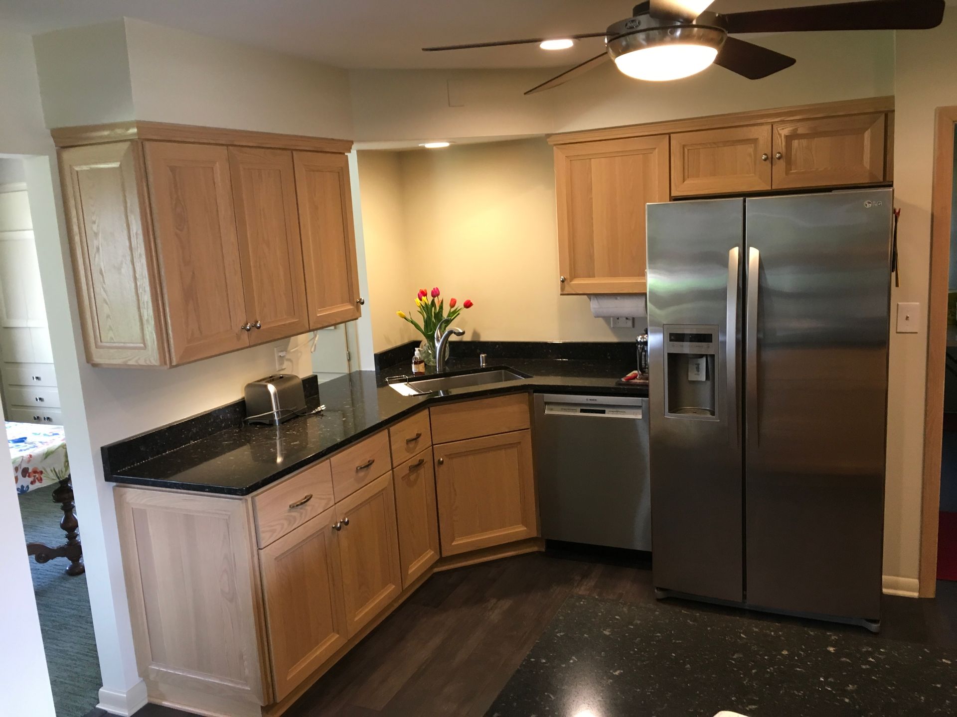 Compact kitchen with wooden cabinets, black countertops, stainless steel appliances, and a ceiling fan.
