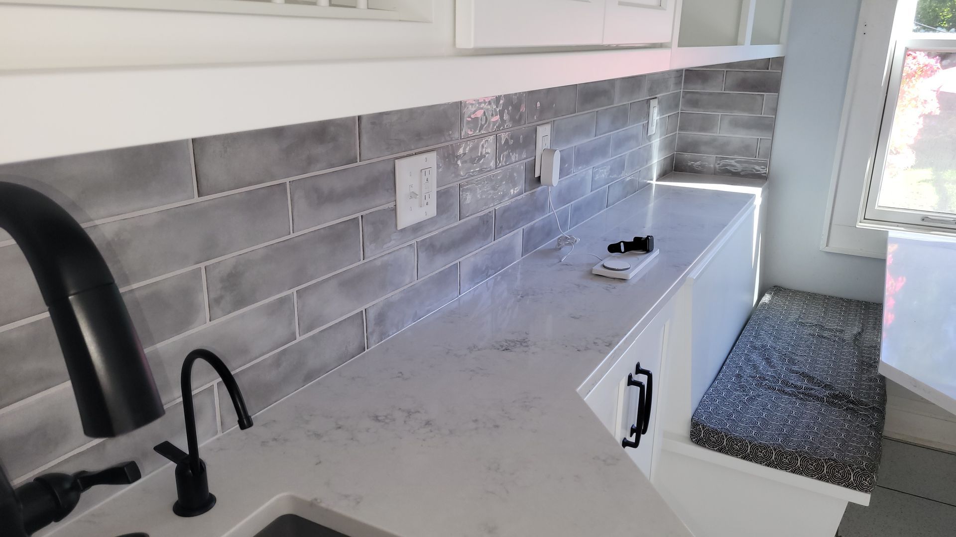 Modern kitchen counter with gray subway tile backsplash, white cabinets, sink faucet, and a doorway with rug.