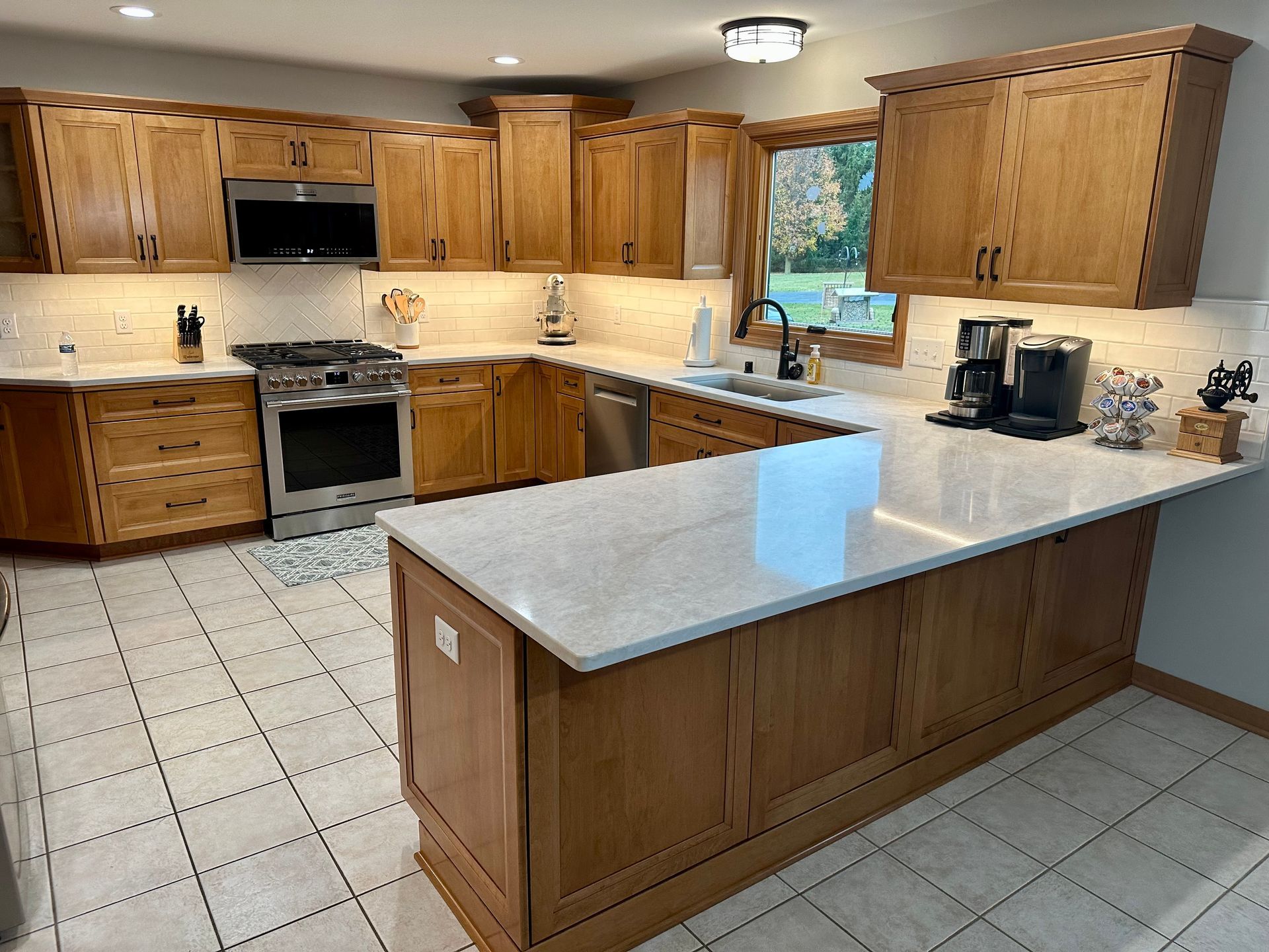 Bright kitchen with wood cabinets, white tile floor, and a large center island with light countertop.