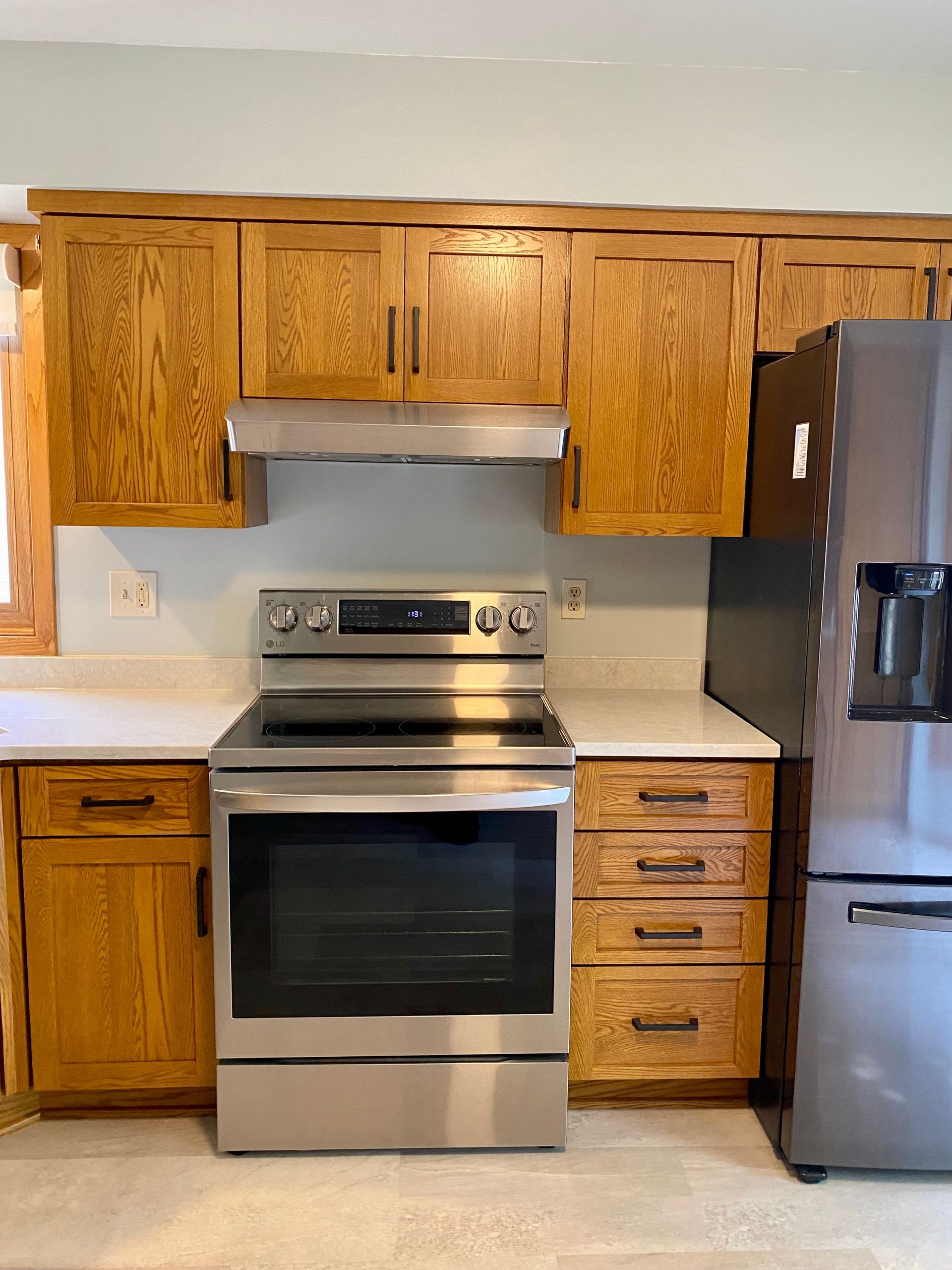 Kitchen with wooden cabinets, stainless steel stove and refrigerator, and light countertop.