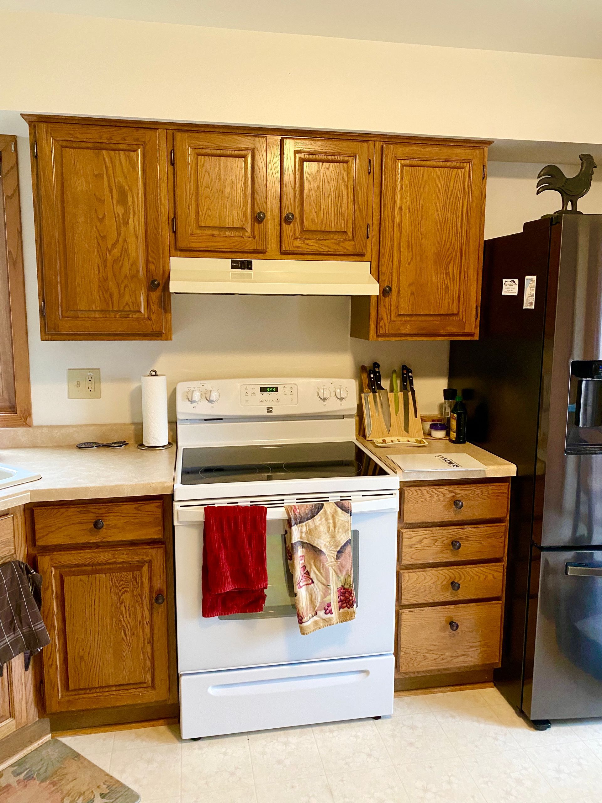 Kitchen with wooden cabinets, white stove, and black refrigerator, with towels hanging on the oven door.