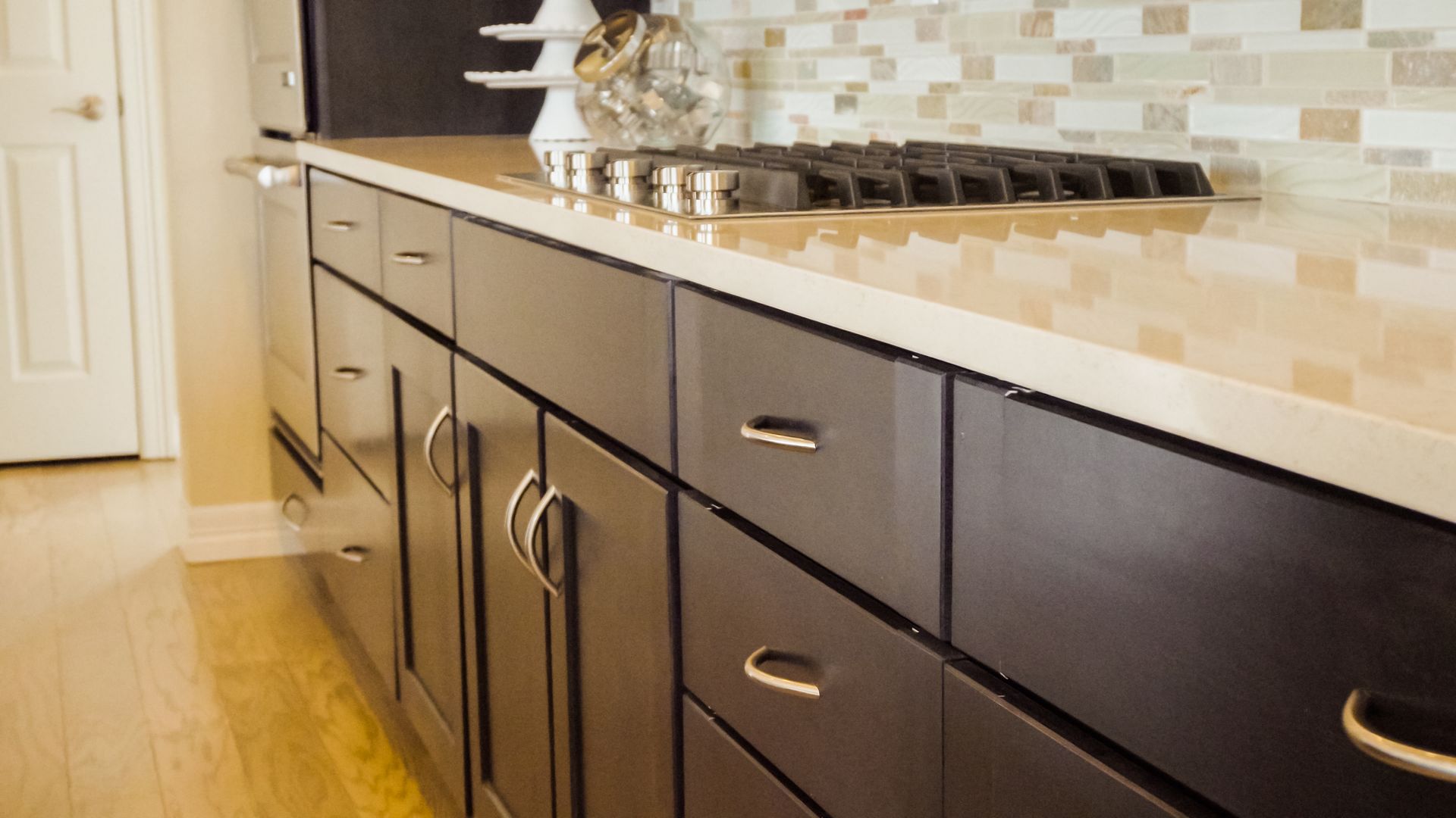 Modern kitchen with dark cabinets, stainless gas cooktop, and glossy countertop.