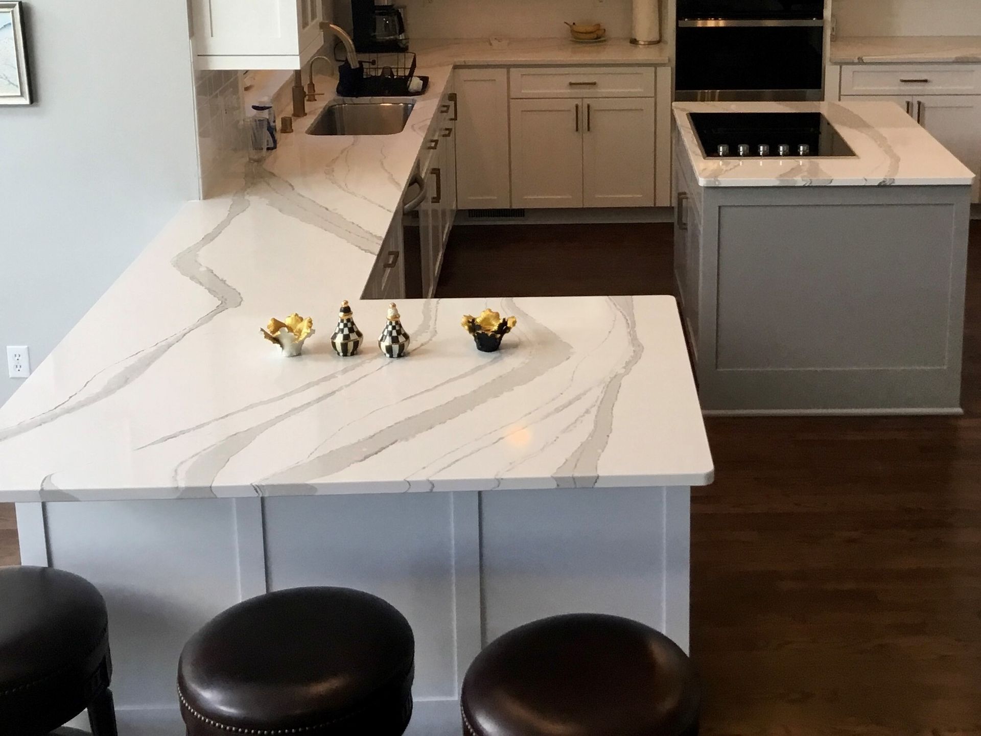 Modern kitchen with white marble island, dark stools, and built-in stove and cabinetry