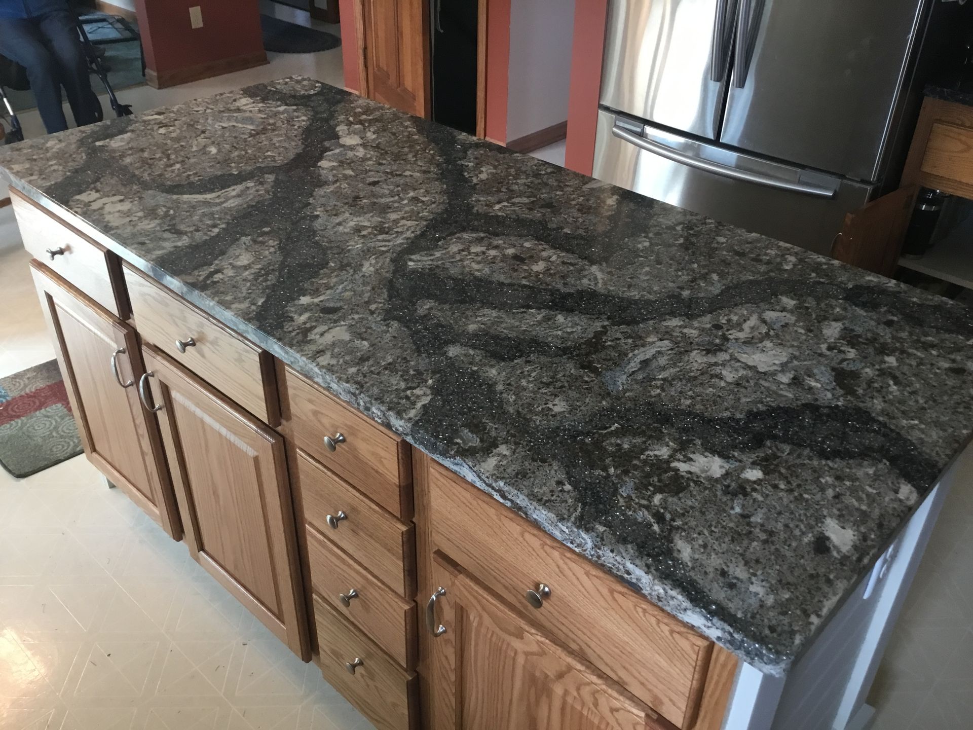 Granite kitchen island countertop with dark speckled pattern and wood cabinets beneath