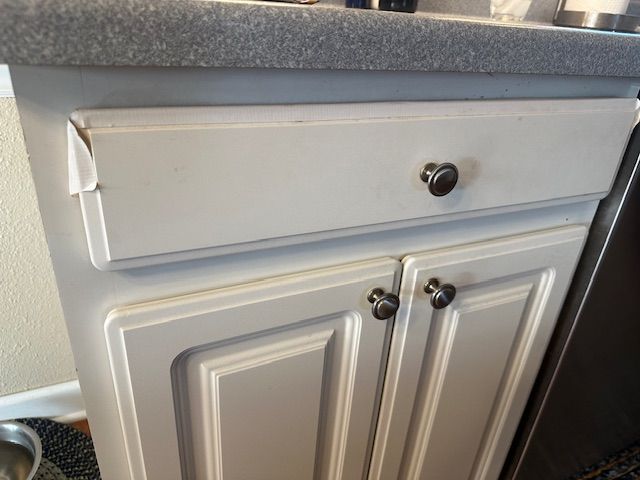 White kitchen cabinet with a drawer and two doors, gray countertop.