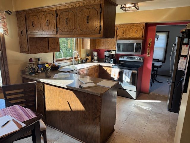 Compact kitchen with wood cabinets, white island, stove, microwave, sink, and tiled floor under a window