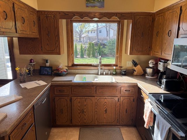 Wood-paneled kitchen with sink under a window, beige counters, and black stove and microwave