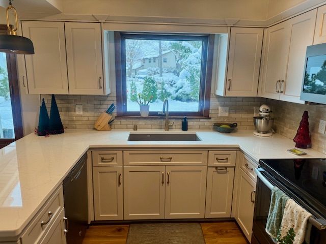 Bright kitchen with white cabinets, beige countertops, and a window over the sink overlooking greenery.
