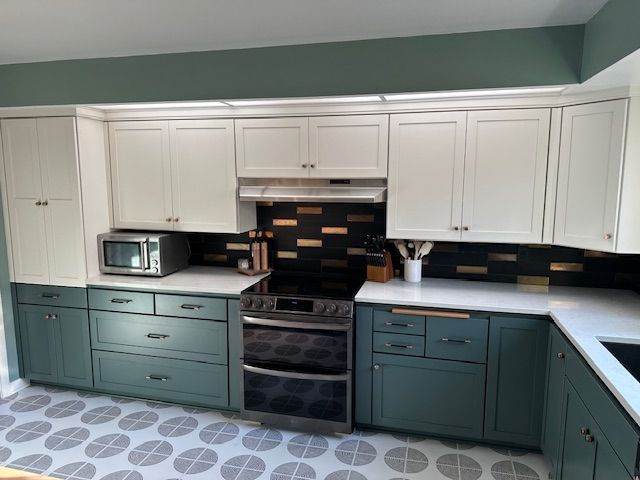 Modern kitchen with white upper cabinets, teal lower cabinets, black backsplash, and stainless appliances