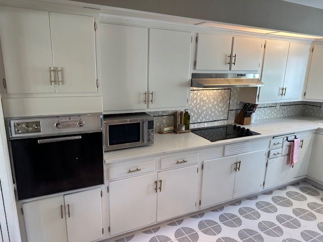 Bright white kitchen with cabinets, black appliances, and a patterned gray floor rug