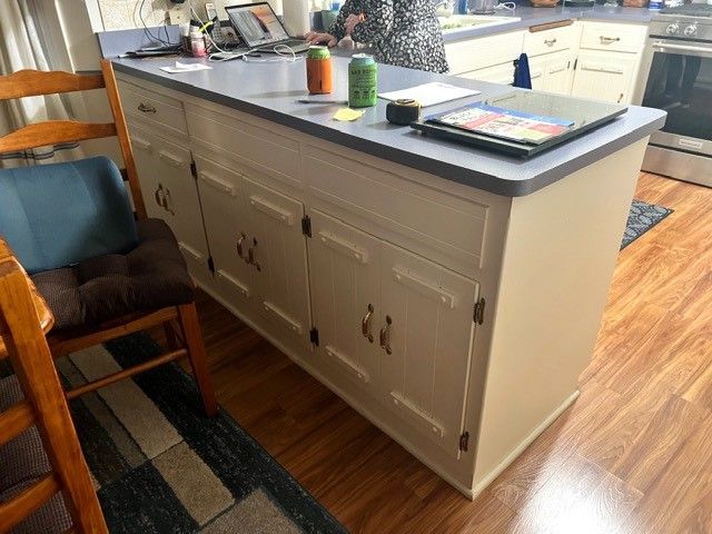 Kitchen island with dark countertop, white cabinets, and chairs beside it in a bright room