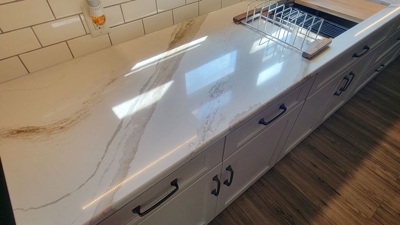 White kitchen countertop with sink, chrome faucet, and drawers beside a tiled backsplash and wood floor