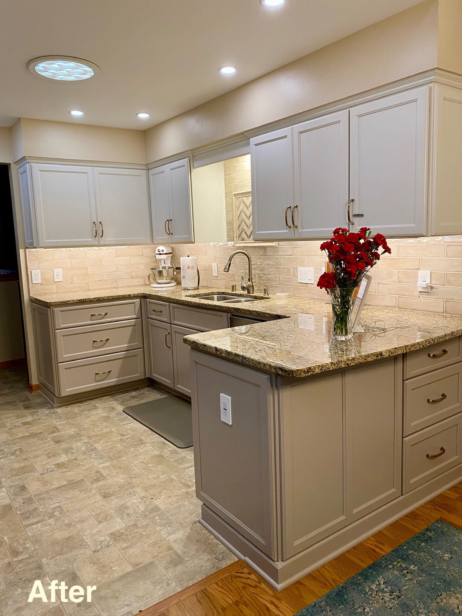 Updated kitchen with gray cabinets, granite countertops, and a vase of red flowers on the island.