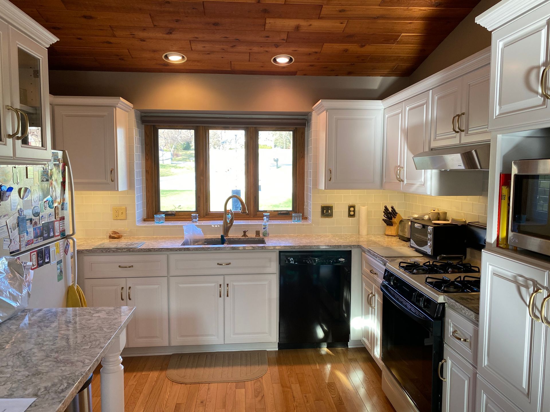 Bright kitchen with white cabinets, wood ceiling, granite counters, stainless appliances, and a window above the sink