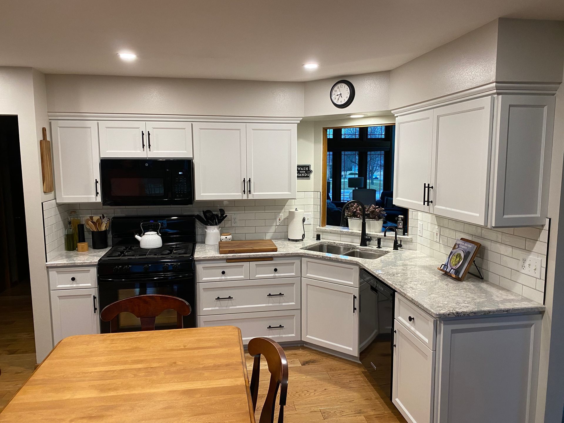Bright kitchen with white cabinets, black appliances, and a wooden table in the foreground.