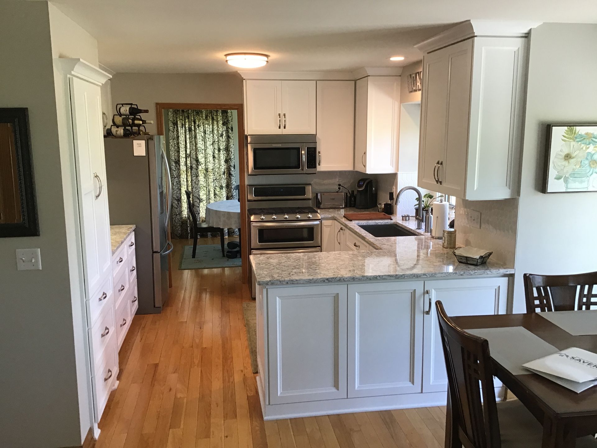 Kitchen with white cabinets, granite island, stainless appliances, and a dining nook beyond hardwood floors