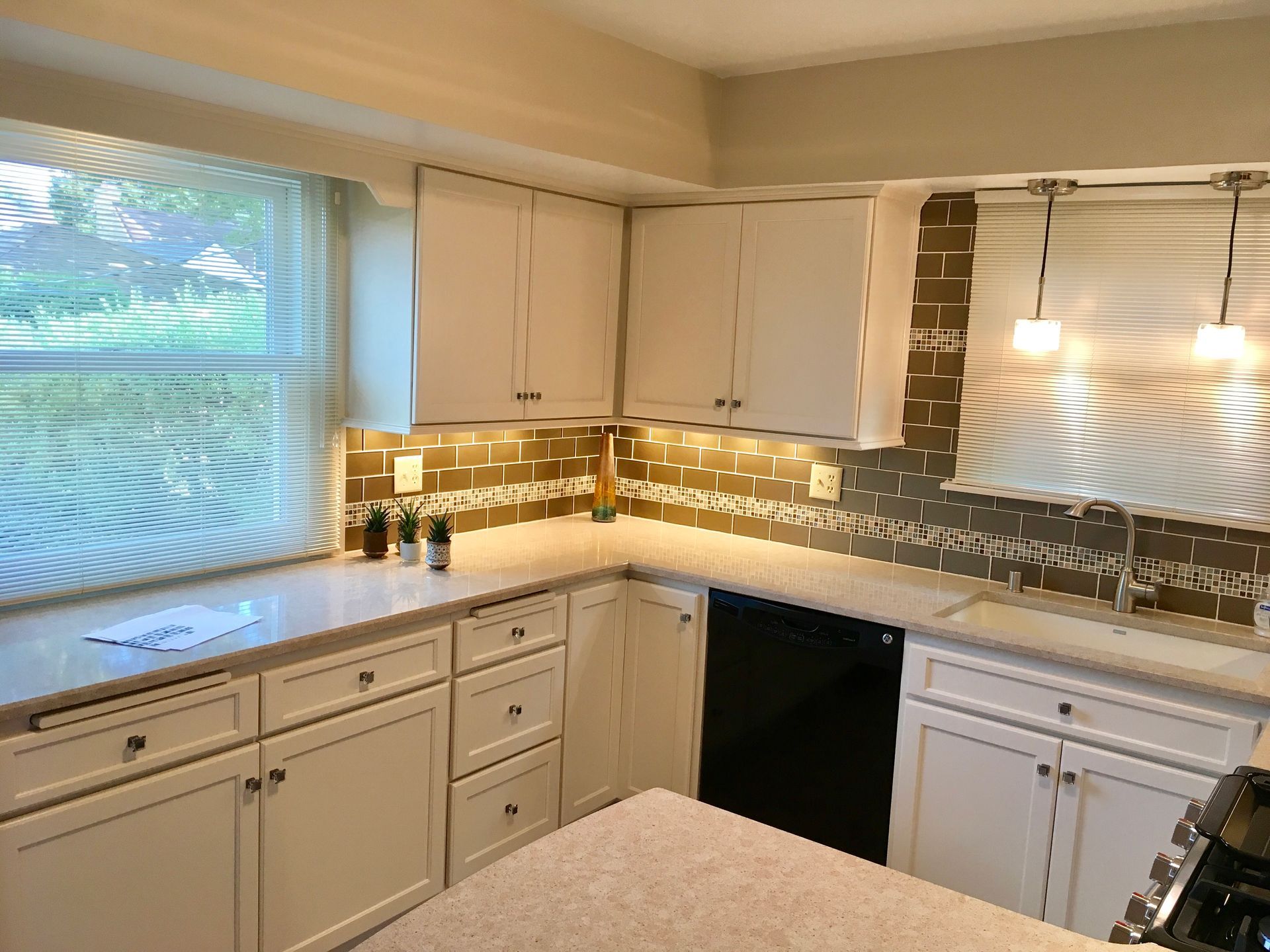 Bright white kitchen with cabinets, window, mosaic backsplash, and pendant lights over the counter