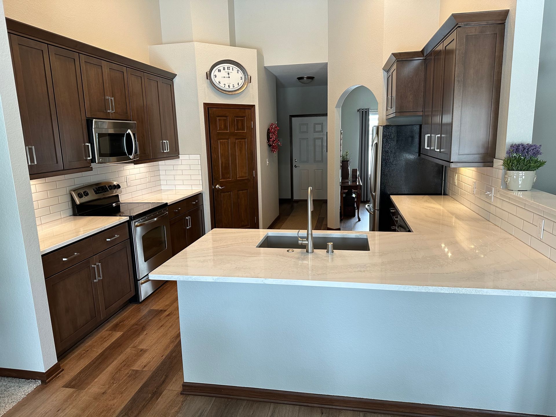 Modern kitchen with dark wood cabinets, white countertops, and a central island with sink and faucet.