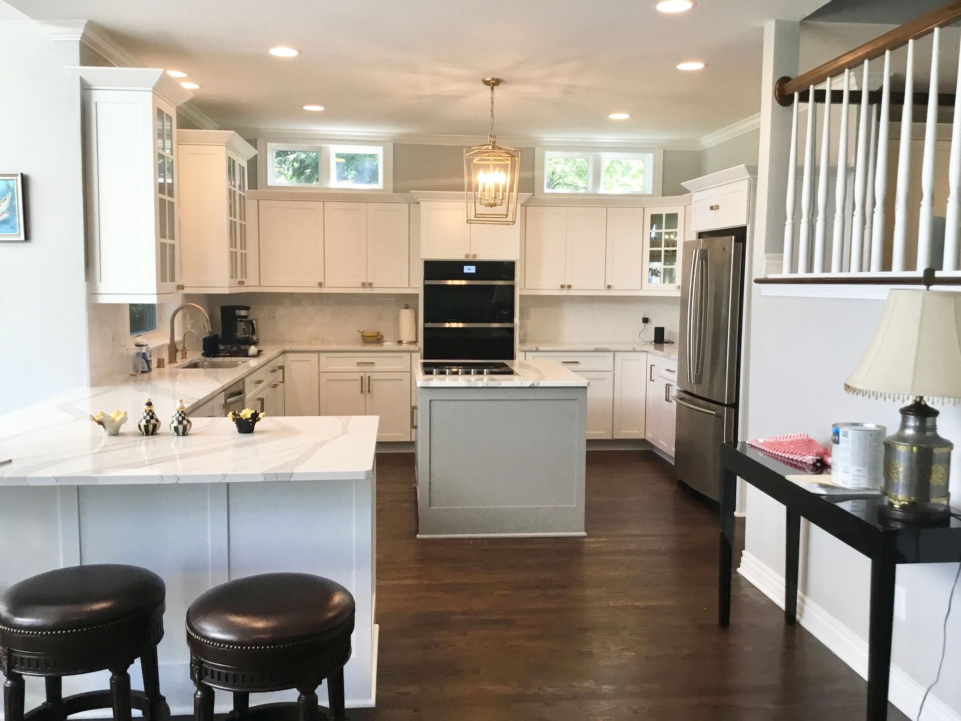 Bright white kitchen with island, stools, stainless appliances, and dark wood floor