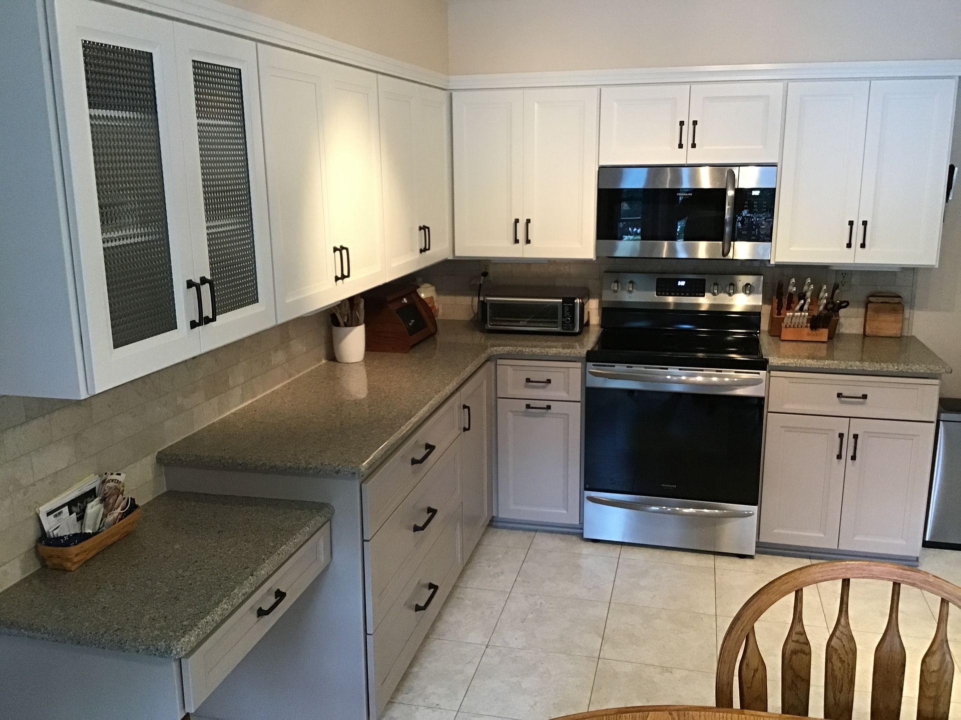 Bright kitchen with white cabinets, stainless steel stove and microwave, and beige tile floor