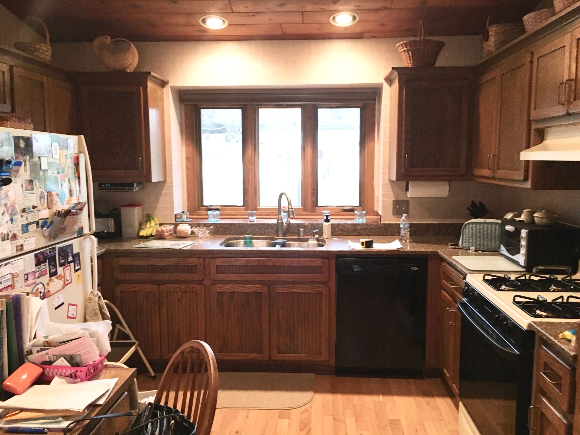 Cozy kitchen with wooden cabinets, a window over the sink, and a cluttered refrigerator on the left.
