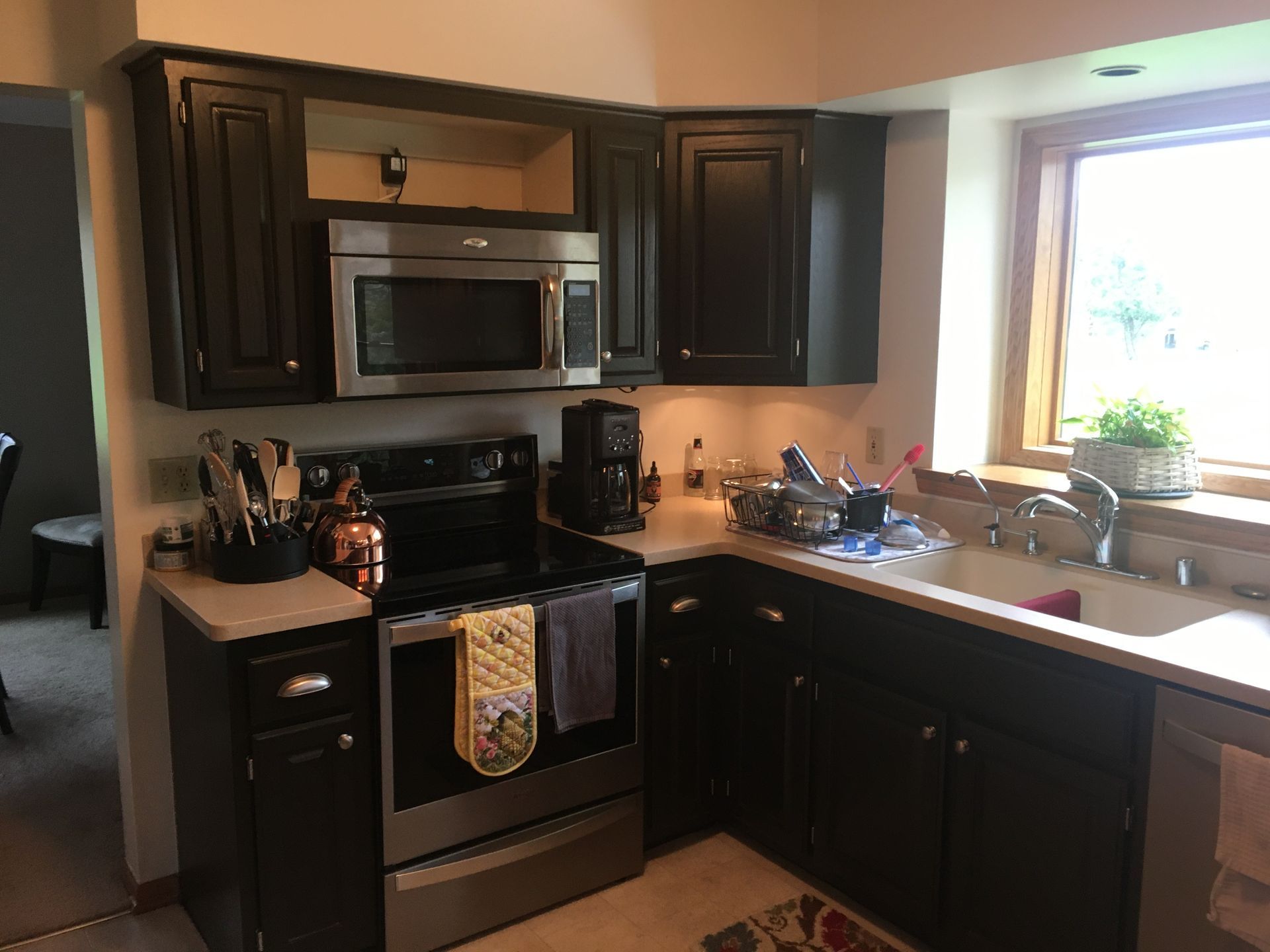 Kitchen with dark cabinets, stainless steel stove and microwave, and a bright window over the sink.