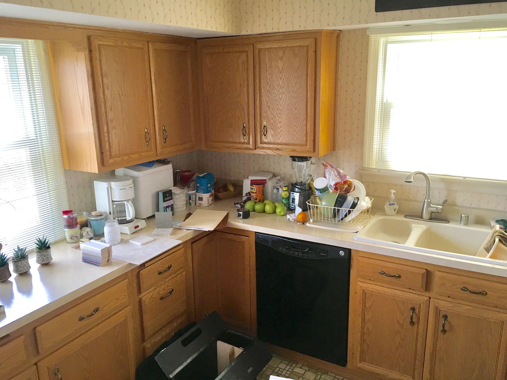Kitchen interior with wooden cabinets, white countertops, sink, dishwasher, and sunlight through the windows