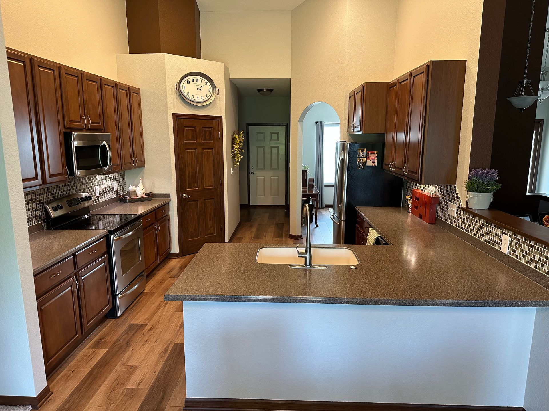 Kitchen with wood cabinets, granite island, stainless appliances, and a wall clock.